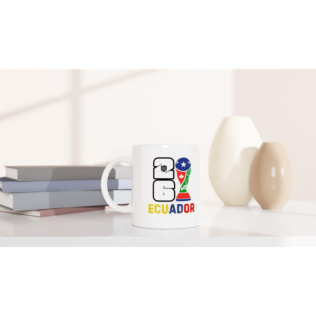 White mug with '2016 Ecuador' text and logo on a white surface with books and decorative items.