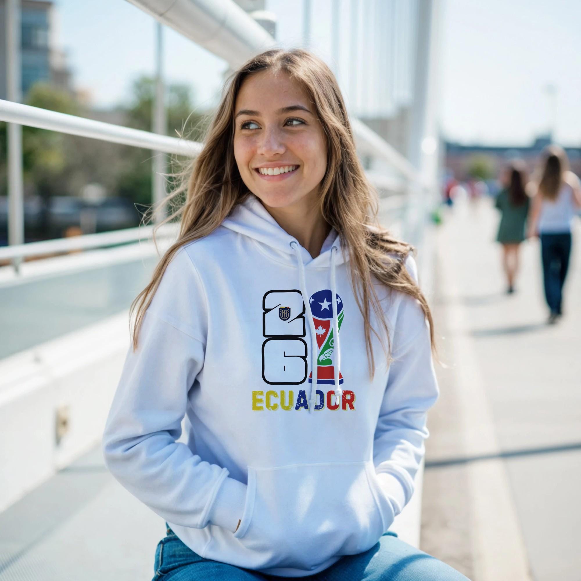 Woman wearing a light blue hoodie with 'Ecuador' text and flag design, sitting outdoors.