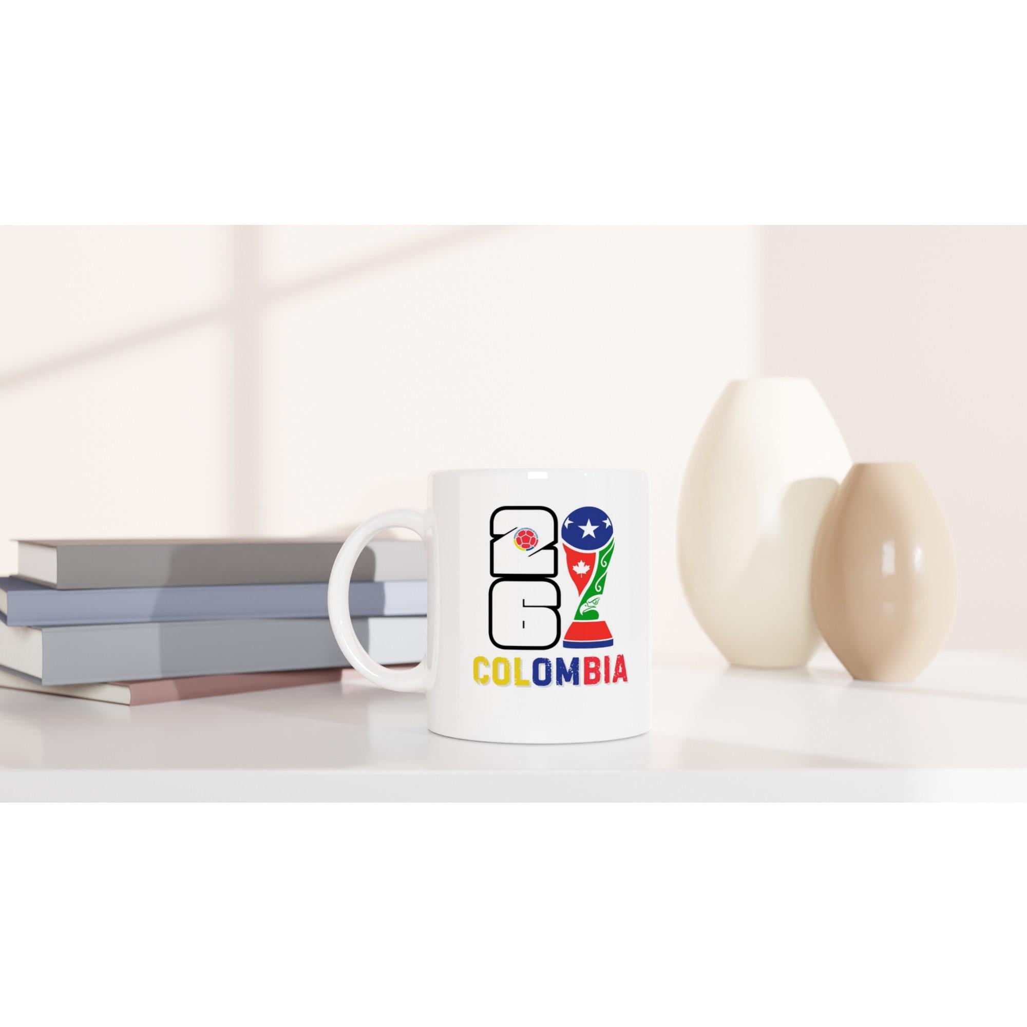 White mug with '2061 Colombia' design on a white surface with books and decorative items.