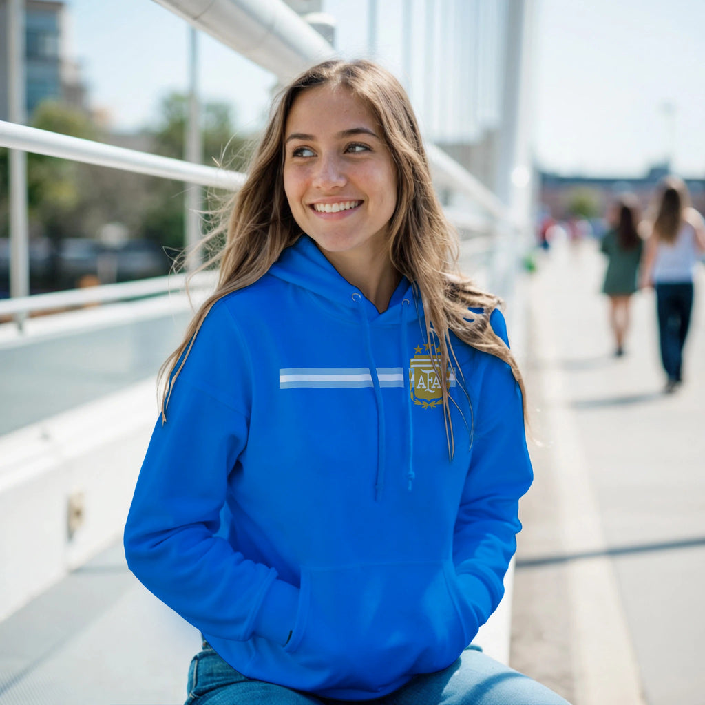 Woman wearing a blue hoodie with a logo, sitting outdoors on a sunny day.