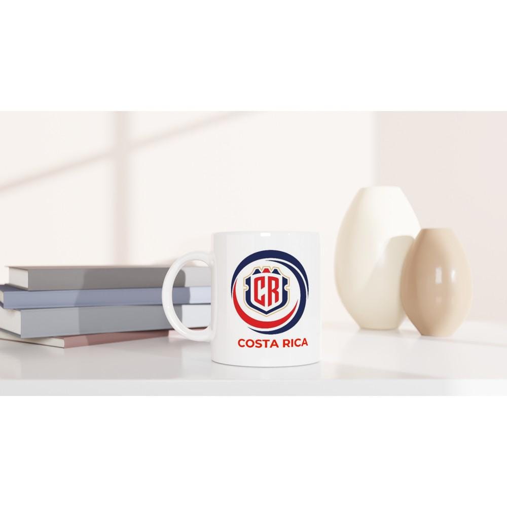 White mug with Costa Rica logo on a white surface with books and decorative items.